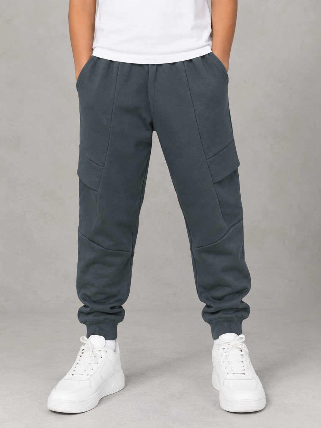 A person wearing dark slate gray jogger sweatpants with cargo pockets, paired with a white t-shirt and white sneakers, standing against a neutral gray background.