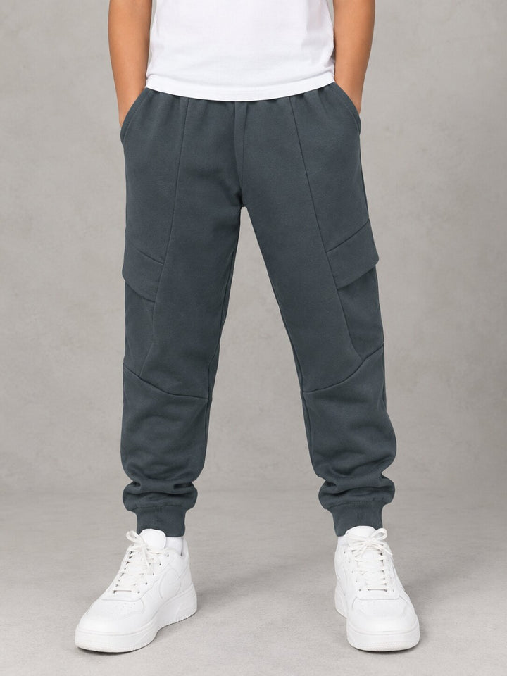 A person wearing dark slate gray jogger sweatpants with cargo pockets, paired with a white t-shirt and white sneakers, standing against a neutral gray background.
