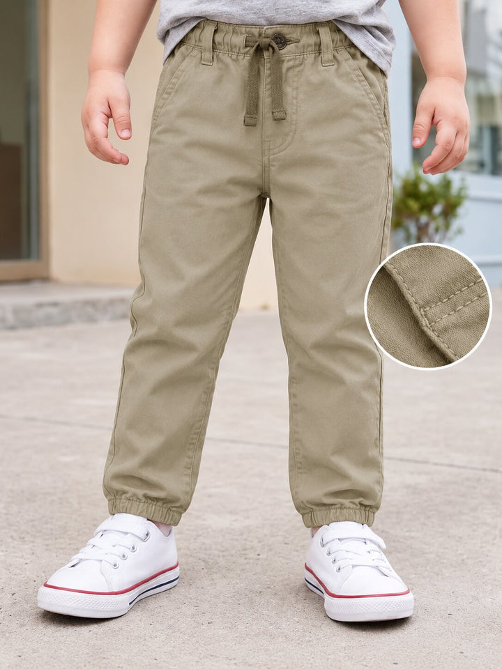Toddler wearing khaki drawstring pants with elastic cuffs, paired with white sneakers, shown outdoors with a circular inset detail of the fabric texture.
