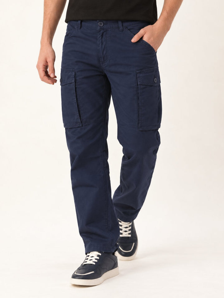 A person wearing navy blue cargo pants with side flap pockets, paired with a black t-shirt and navy sneakers, shown from the waist down on a light studio background.