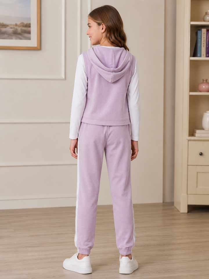 A child model shown from the back wearing a lavender hooded sweatshirt vest over a white long-sleeve top, paired with matching lavender jogger sweatpants with white side stripes and white sneakers, in a bright indoor room.