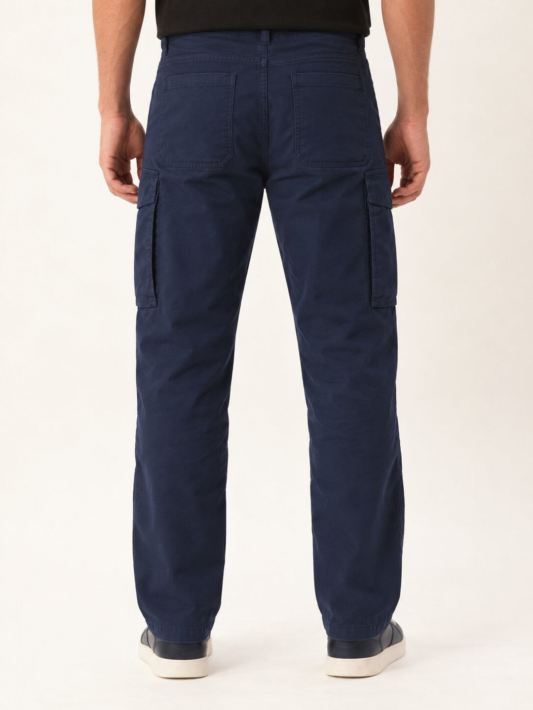 A person shown from the back wearing dark navy cargo pants, a black top, and white sneakers against a plain light background.