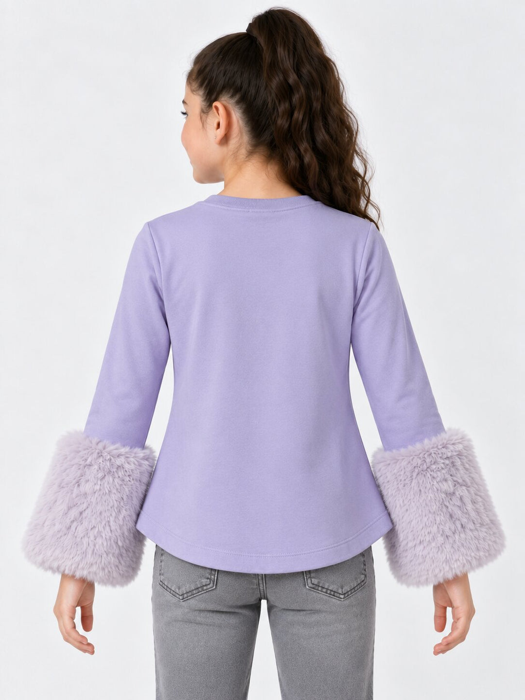 A woman shown from the back wearing a lavender long-sleeve top with fluffy faux-fur cuffs, paired with gray jeans, against a plain white studio background.