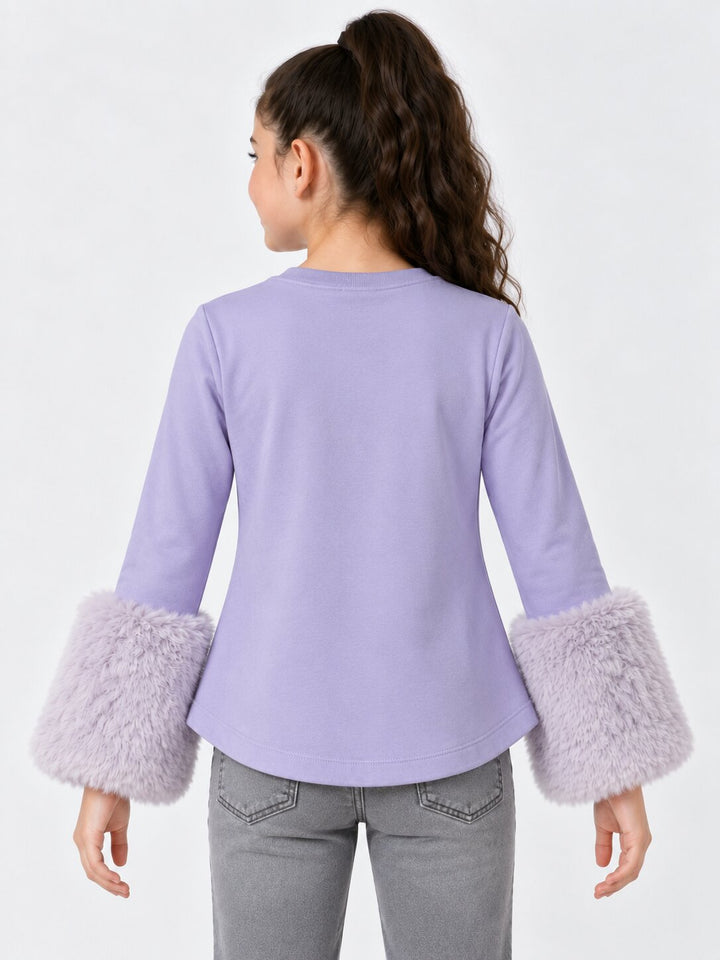 A woman shown from the back wearing a lavender long-sleeve top with fluffy faux-fur cuffs, paired with gray jeans, against a plain white studio background.