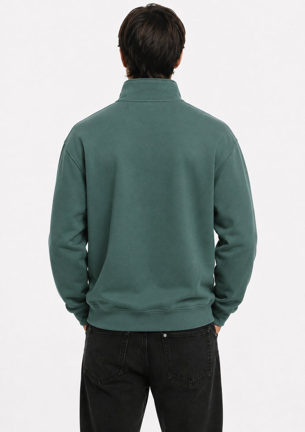 A man viewed from behind wearing a dark green mock neck sweatshirt and black jeans against a plain white studio background.