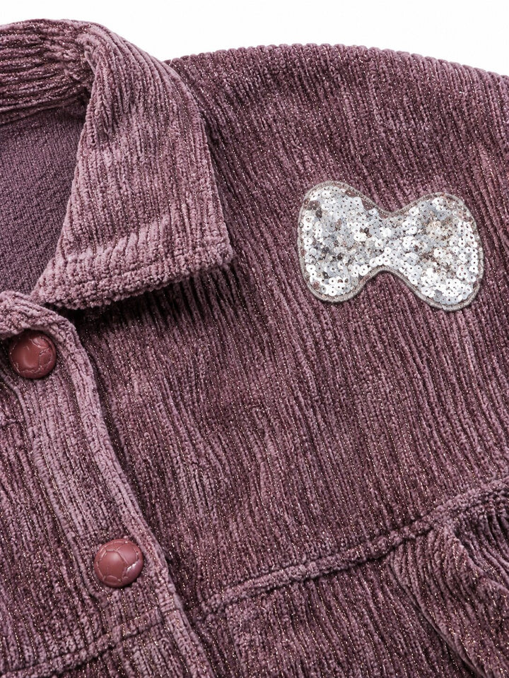 Close-up of a textured corduroy button-up shirt in a dusty mauve-purple color, featuring a silver glitter bow pin on the chest pocket.