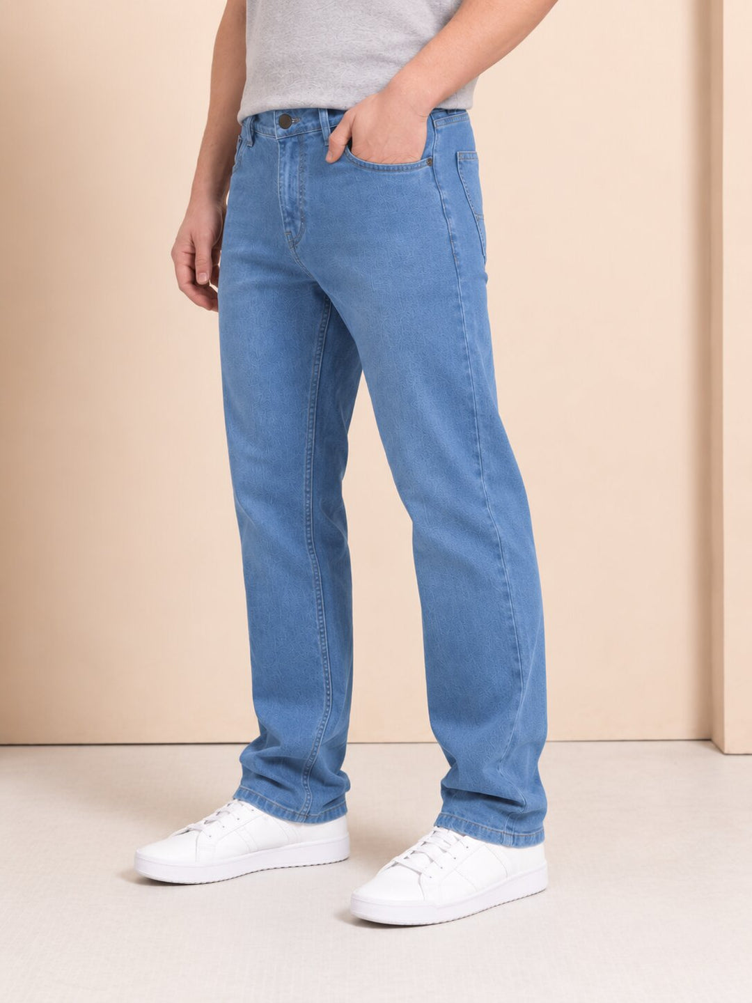 A person wearing light blue straight-leg denim jeans, a light gray t-shirt, and white sneakers, standing against a beige studio background.