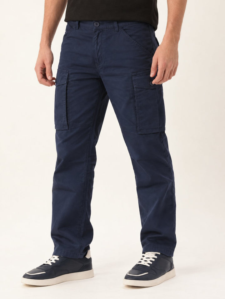 A person wearing dark navy cargo pants with side flap pockets, paired with a black t-shirt and navy sneakers with white soles, photographed against a clean off-white studio background.