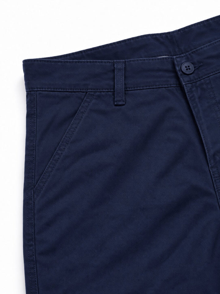 Close-up of navy blue trousers showing the waistband, belt loops, button, and side pocket stitching on a white background.