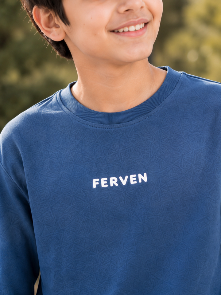 A close-up of a person wearing a blue crewneck sweatshirt with the word 'FERVEN' printed in white on the chest, set against a blurred outdoor background.