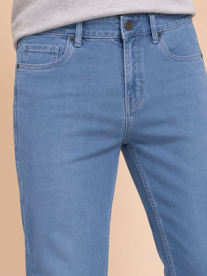 Close-up of a person wearing light blue denim jeans with a gray top visible at the waist, against a plain beige studio background.