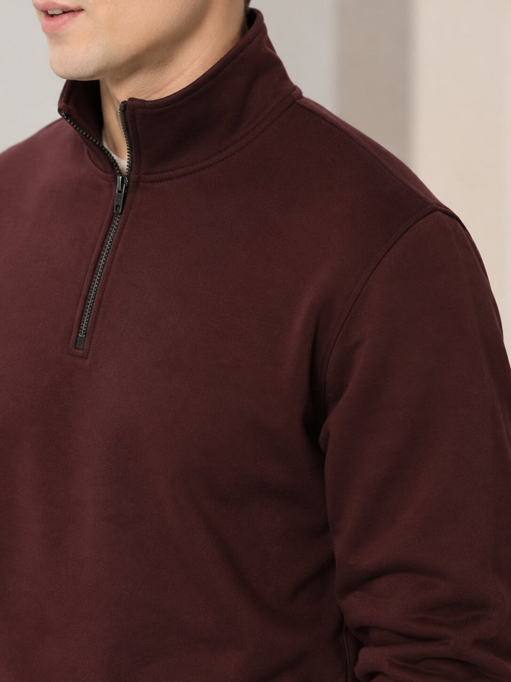 Close-up of a man wearing a dark burgundy quarter-zip pullover sweater, showing the collar, zipper, and fabric texture.