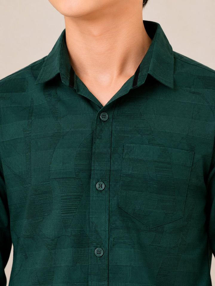 A close-up of a person wearing a dark green textured button-up shirt with a collar and chest pocket, shown from the lower face to the torso against a plain light beige background.