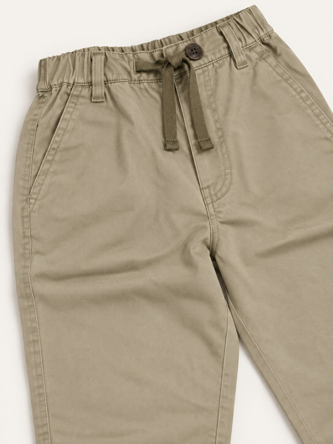 A close-up of a pair of khaki drawstring trousers, showing the elastic waistband, button closure, and fabric texture against a plain white background.