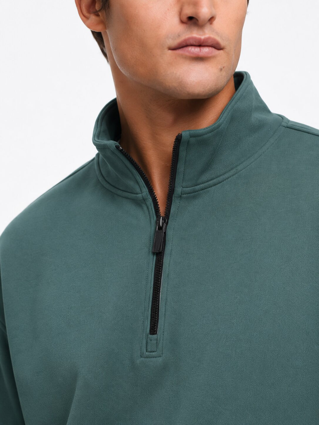 Close-up of a man wearing a muted teal-green quarter-zip pullover sweatshirt against a plain white background.