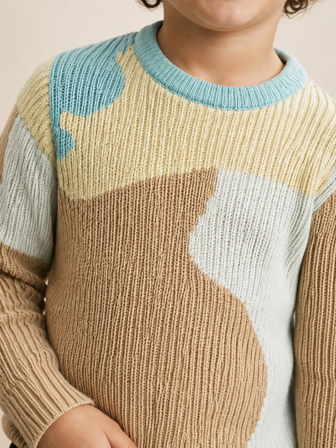 A close-up of a child wearing a ribbed knit sweater with large abstract color blocks in beige, tan, light blue, and off-white.