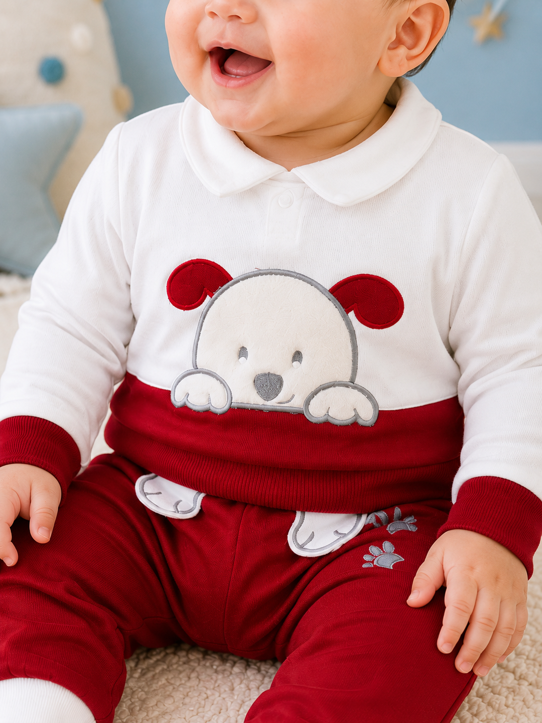 A baby wearing a red and white two-piece outfit with a white collar long-sleeve top and matching red pants, featuring a cartoon dog graphic on the front.