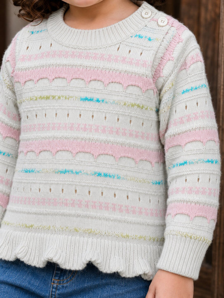 A close-up of a child wearing a cream knit sweater with horizontal pink stripes, scalloped knit trim, and small multicolor dotted accents, paired with blue jeans.