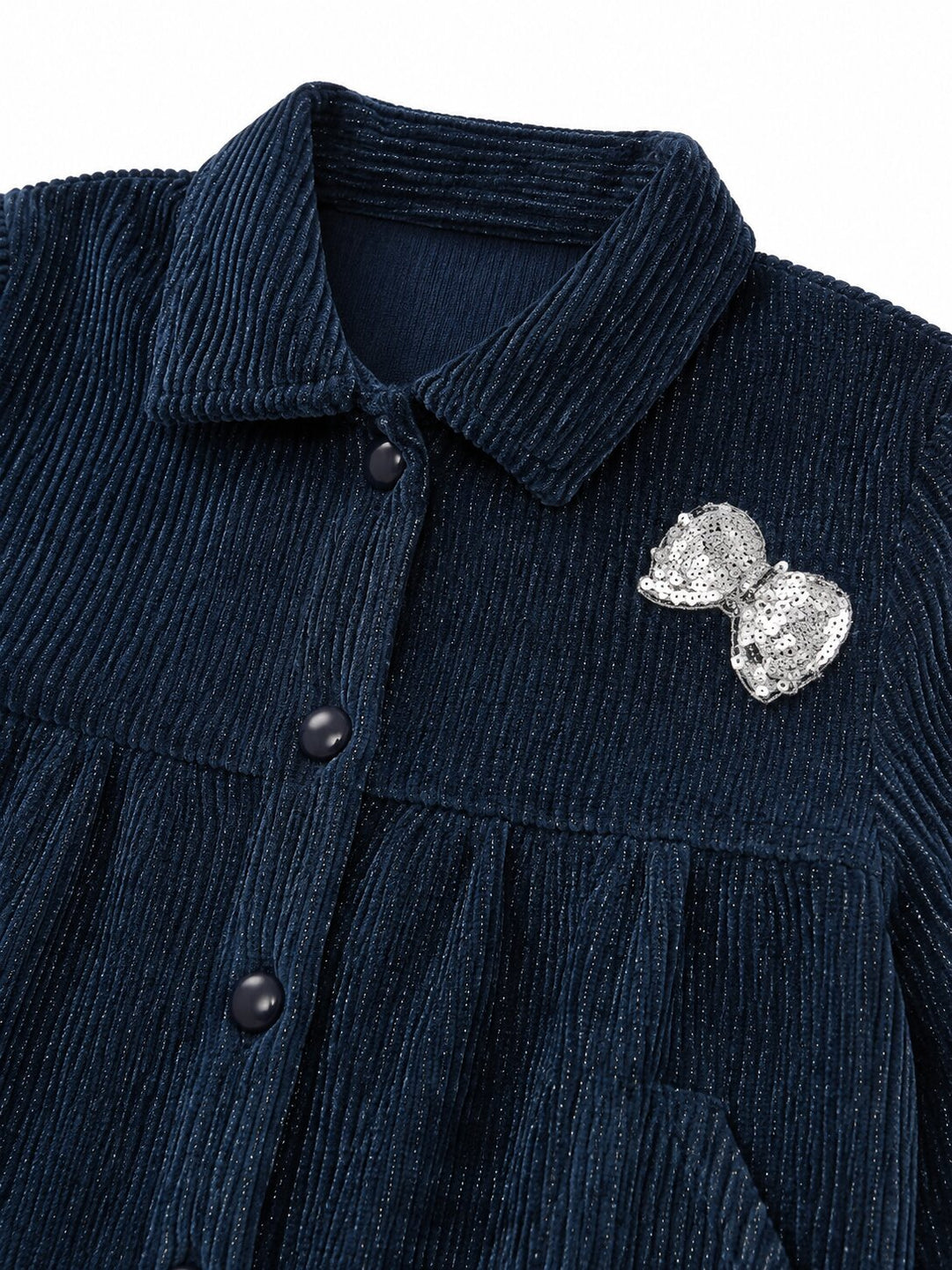 Close-up of a dark navy corduroy button-front garment with a pointed collar and a silver bow-shaped brooch on the chest, shown against a plain white background.