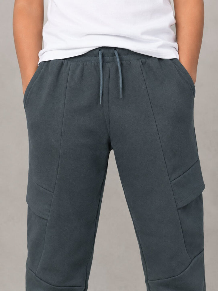 A person wearing dark slate gray drawstring sweatpants with side cargo pockets, paired with a white t-shirt, shown from the chest down against a neutral gray background.