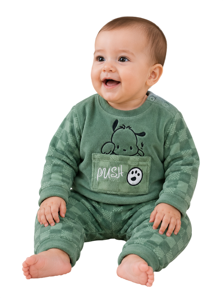 A smiling baby wearing a green patterned footed sleeper with a front pocket that says 'PUSH' and has a cartoon dog graphic, photographed against a plain white background.