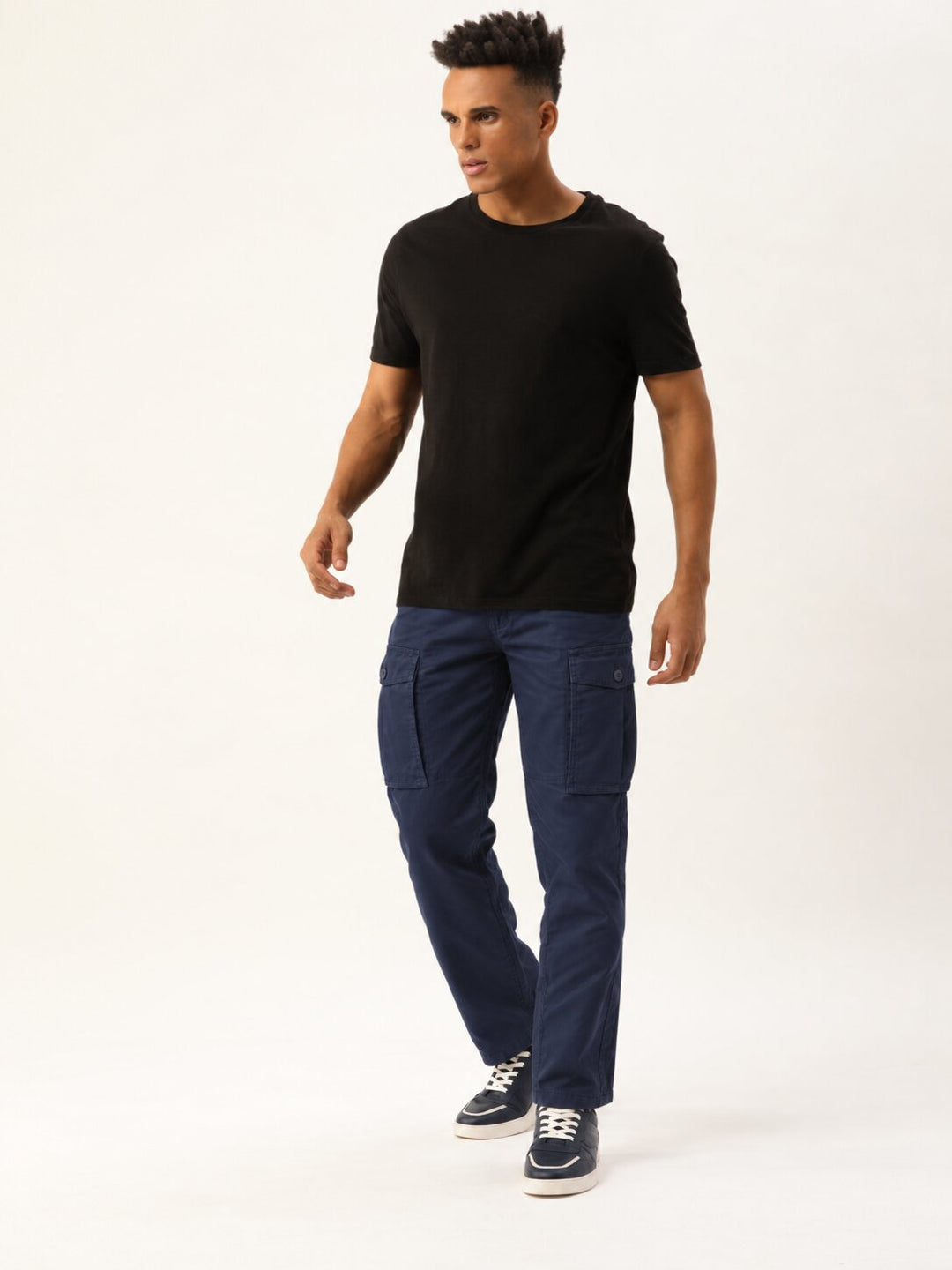 A man modeling a black short-sleeve crewneck t-shirt and dark blue cargo pants with navy sneakers, standing against a plain white studio background.