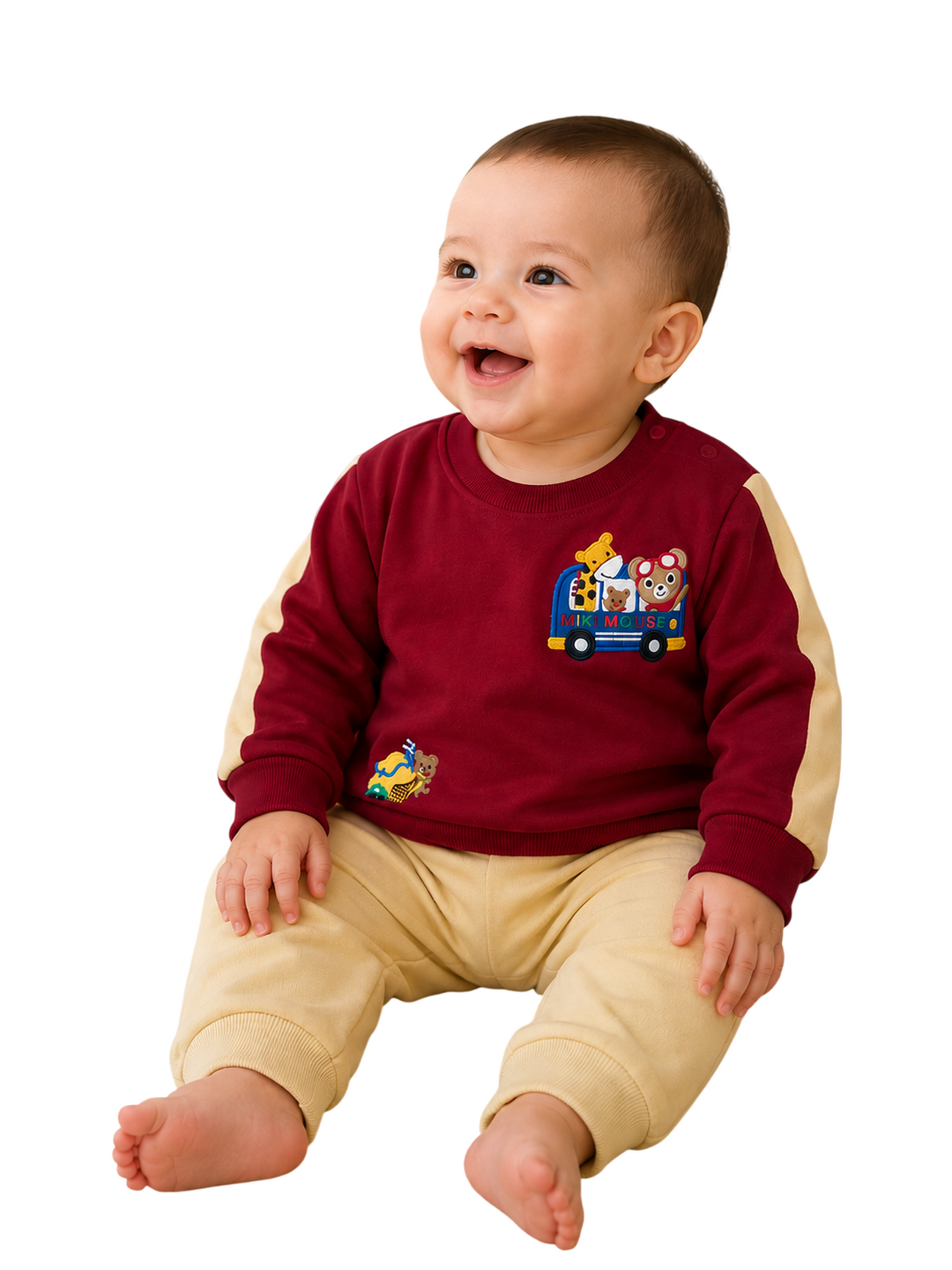 A smiling baby sitting and wearing a burgundy long-sleeve sweatshirt with beige sleeves and a cartoon bus graphic on the chest, paired with beige pants, isolated on a white background.