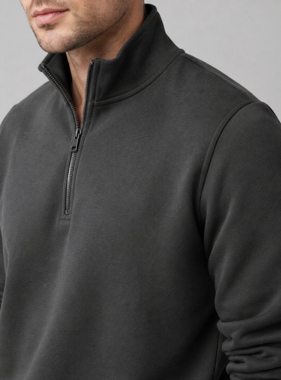 Close-up of a man wearing a dark charcoal gray quarter-zip pullover sweatshirt against a neutral gray background.