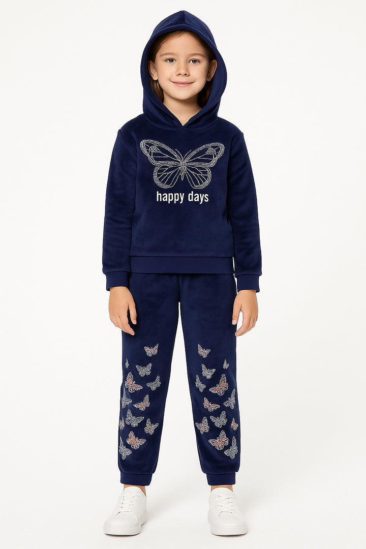 A young girl modeling a navy blue velour tracksuit with butterfly details. The set includes a hooded sweatshirt with a large white butterfly graphic and 'happy days' text on the chest, and matching jogger pants decorated with small butterfly prints.