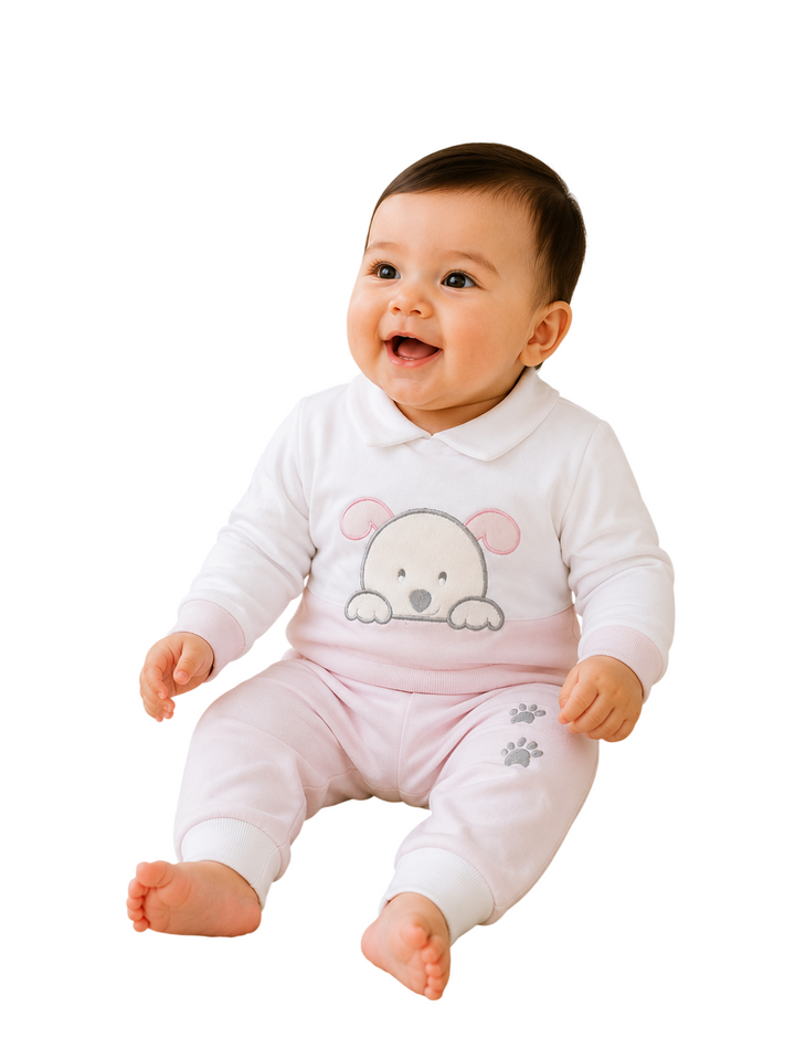 A smiling baby sitting and wearing a white long-sleeve top with a pink bear face graphic and light pink pants with small gray paw prints, isolated on a white background.