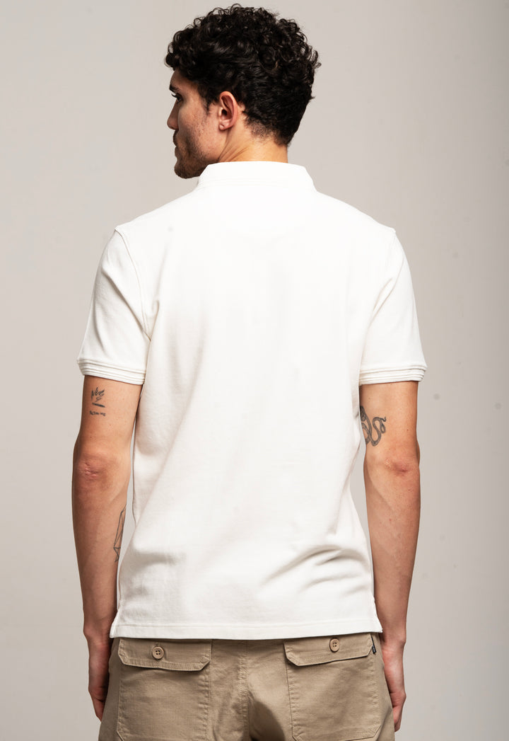 Person wearing a white polo shirt and beige pants against a plain background