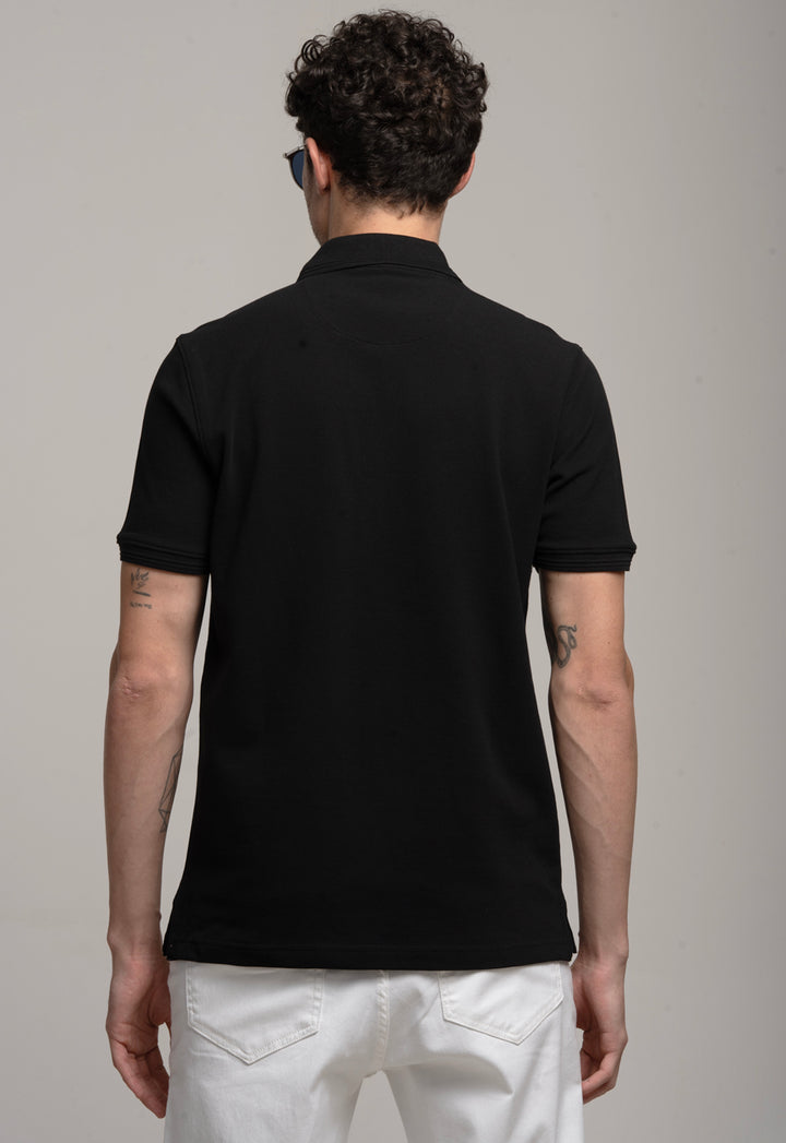 Man wearing a black polo shirt and white pants on a gray background