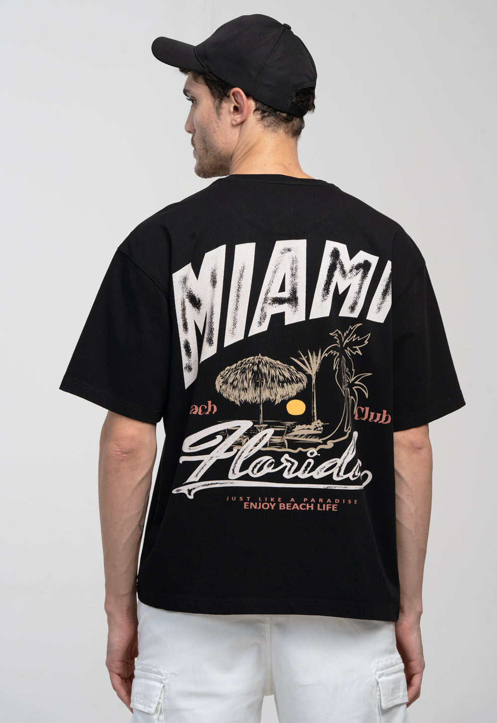 Person wearing a black t-shirt with 'Miami Beach Club' design on the back, standing against a plain background.