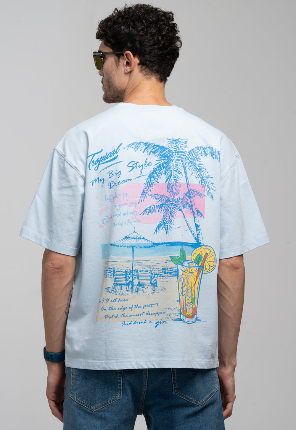 Person wearing a white t-shirt with a tropical design on the back, standing against a plain background.