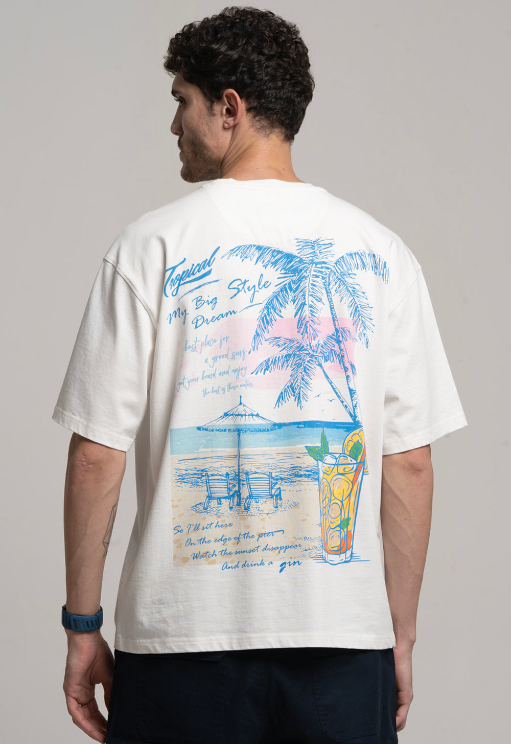 Person wearing a white t-shirt with a colorful beach-themed design on the back.