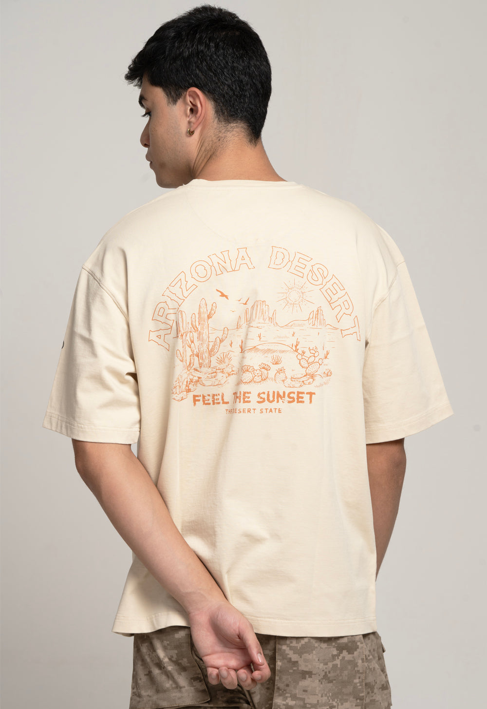 Person wearing a beige t-shirt with a graphic design on the back against a plain background