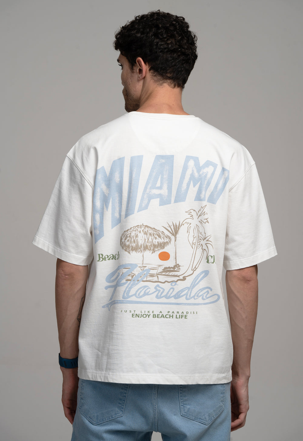 Person wearing a white t-shirt with 'Miami Beach, Florida' design on the back.