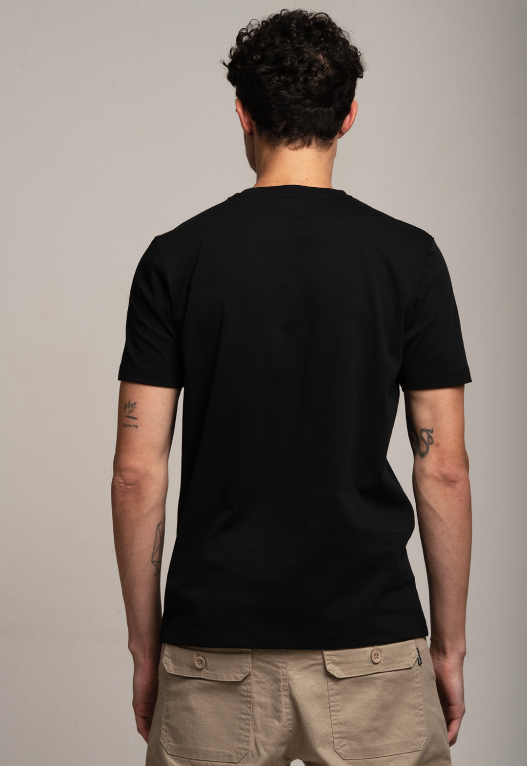 Person wearing a black t-shirt and beige pants against a plain background