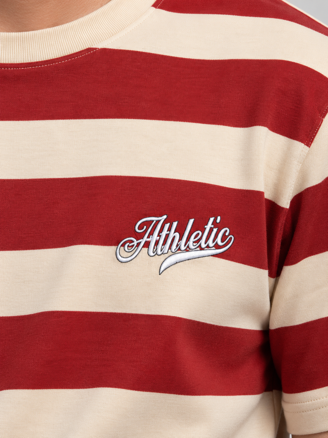 A close-up of a red and cream striped t-shirt featuring a white embroidered 'Athletic' script logo on the chest.