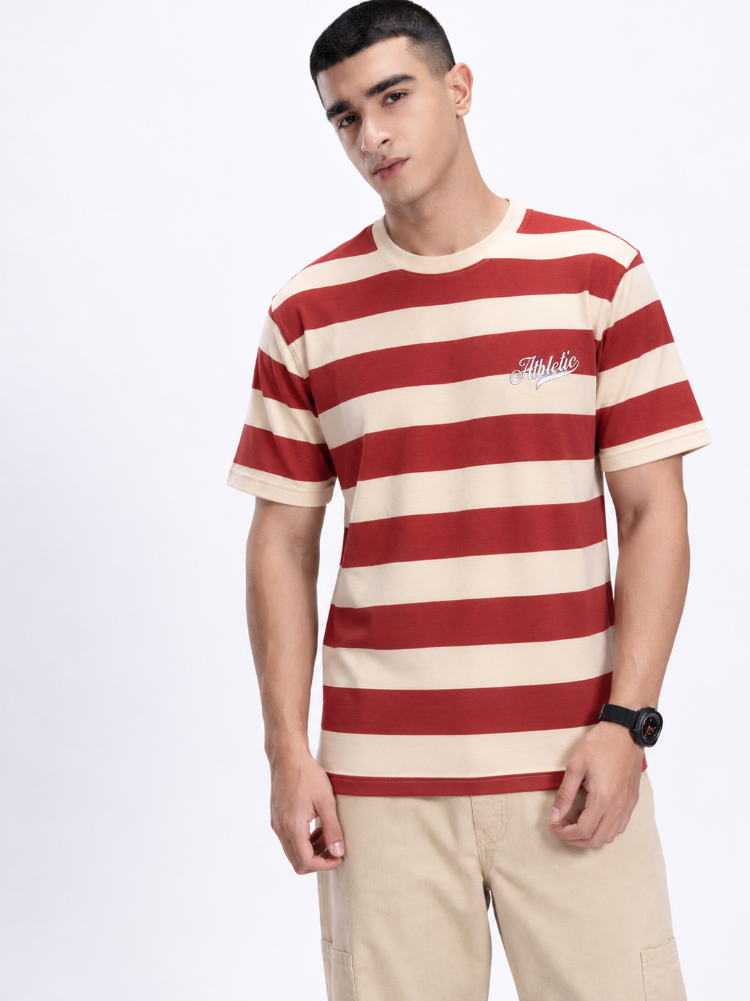 A man wearing a red and cream horizontal striped t-shirt with a small white script logo on the left chest, paired with beige cargo pants, against a plain white studio background.