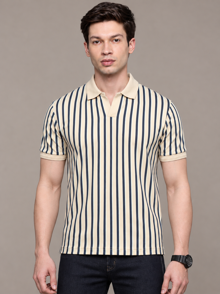 A man wearing a short-sleeve polo shirt with vertical navy blue and cream stripes, paired with dark jeans, standing against a solid gray studio background.