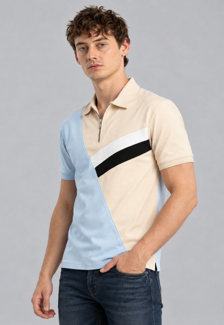 A man wearing a color-blocked polo shirt with light blue, beige, white, and black panels, paired with dark blue jeans, against a solid gray studio background.