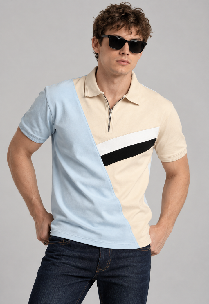A man wearing a color-blocked short-sleeve polo shirt with a quarter-zip collar, dark sunglasses, and dark blue jeans, posed against a solid gray studio background.