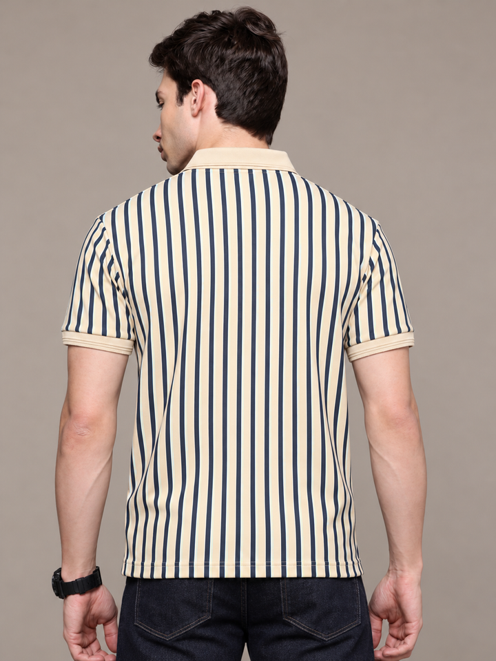 A man viewed from behind wearing a short-sleeve polo shirt with vertical navy blue and cream stripes, paired with dark jeans, against a solid taupe background.