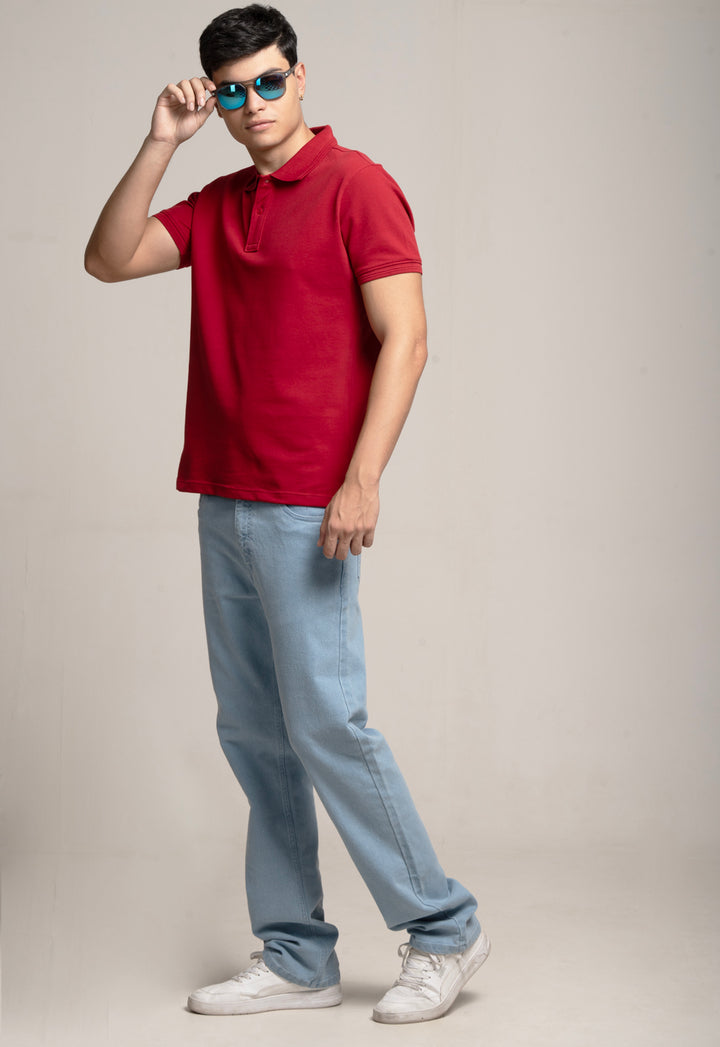 Man wearing a red polo shirt, light blue jeans, and white sneakers on a plain background