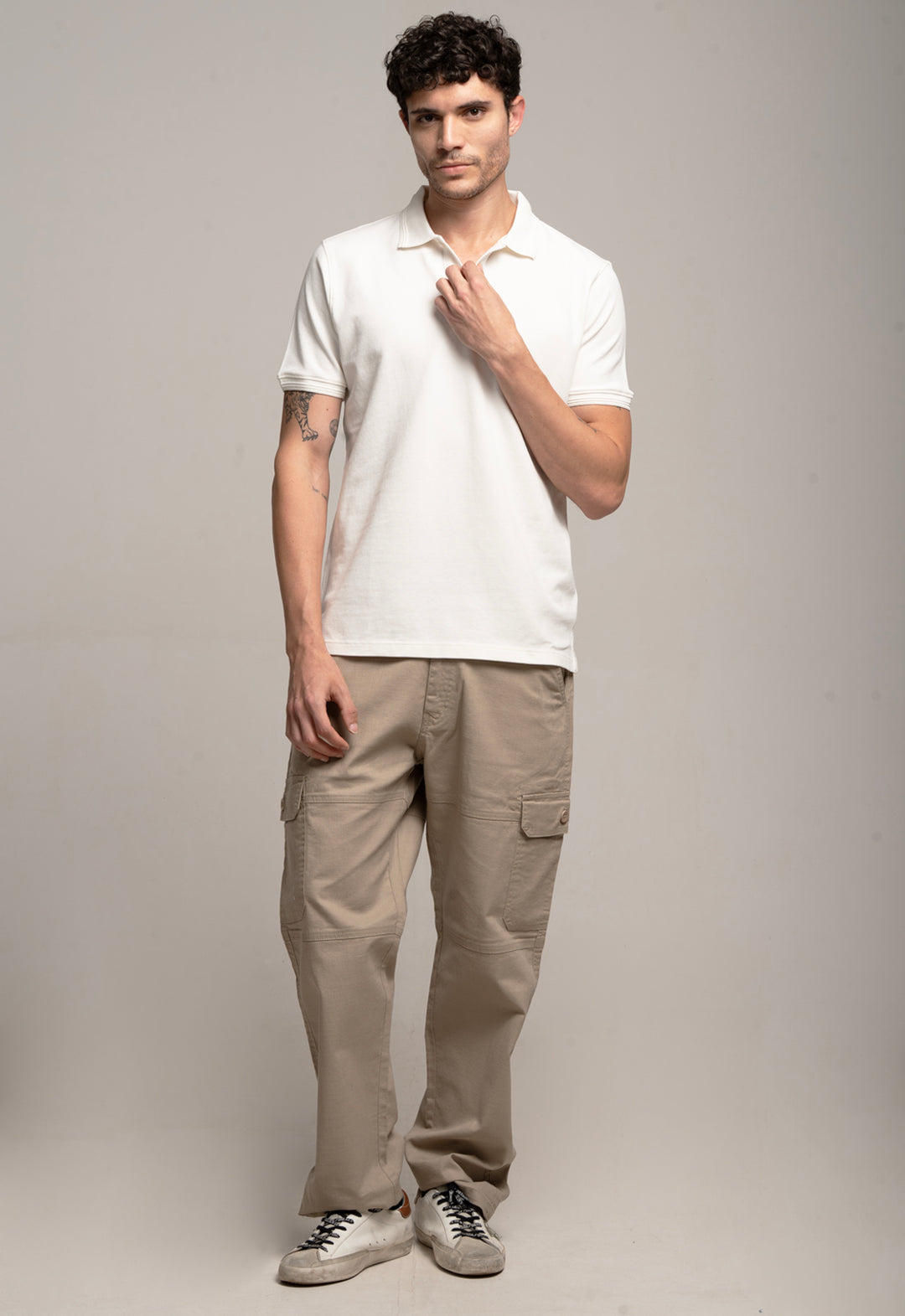 Man wearing a white polo shirt and beige pants against a gray background