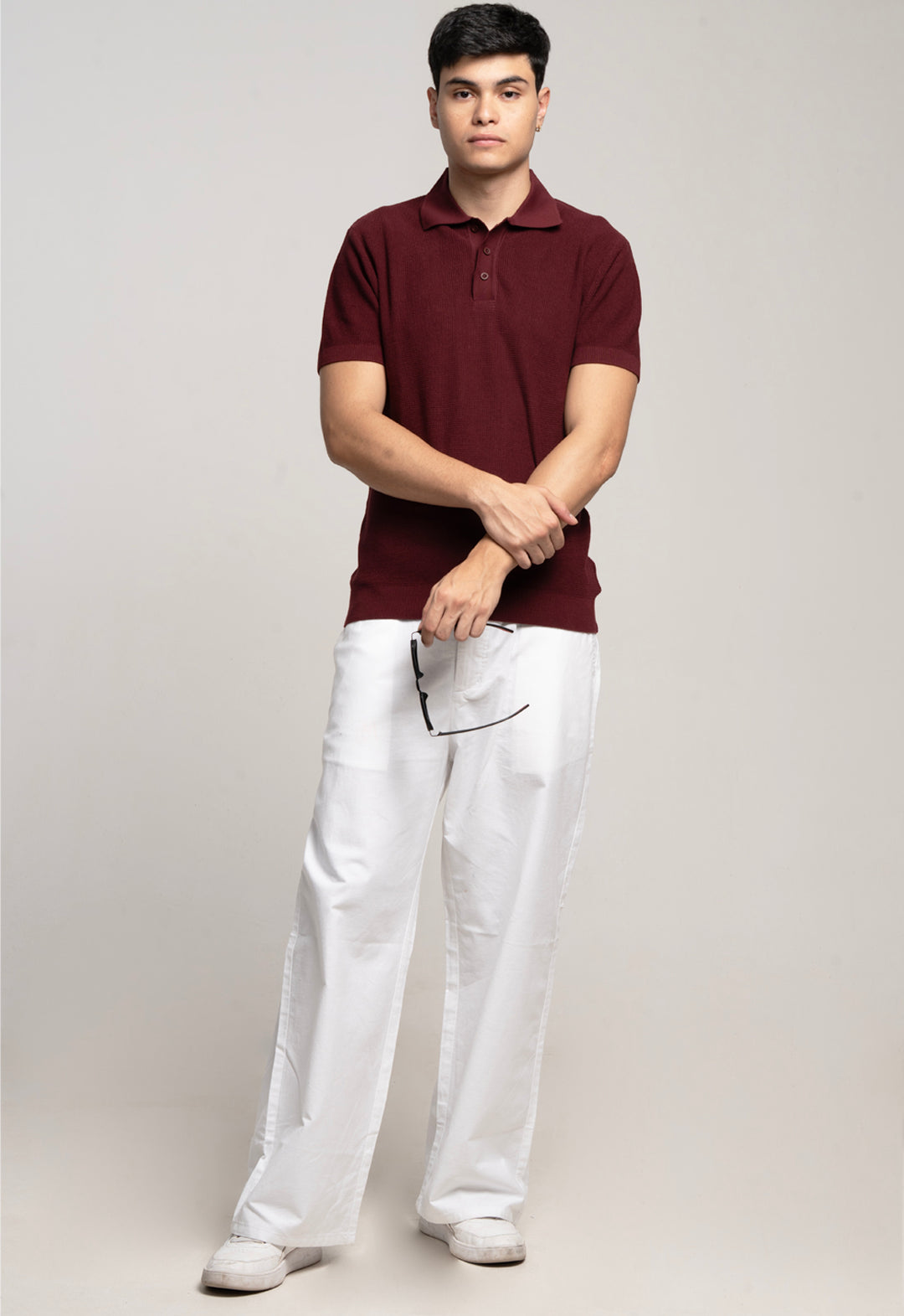 Man wearing a maroon polo shirt and white pants on a plain background