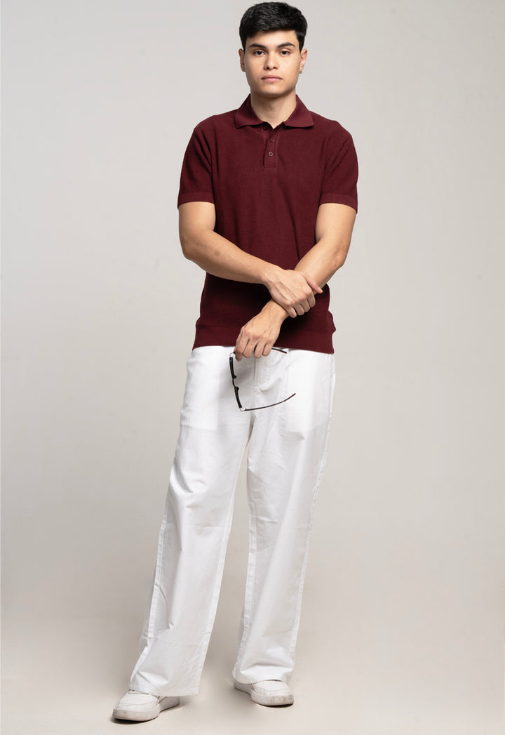 Man wearing a maroon polo shirt and white pants on a plain background
