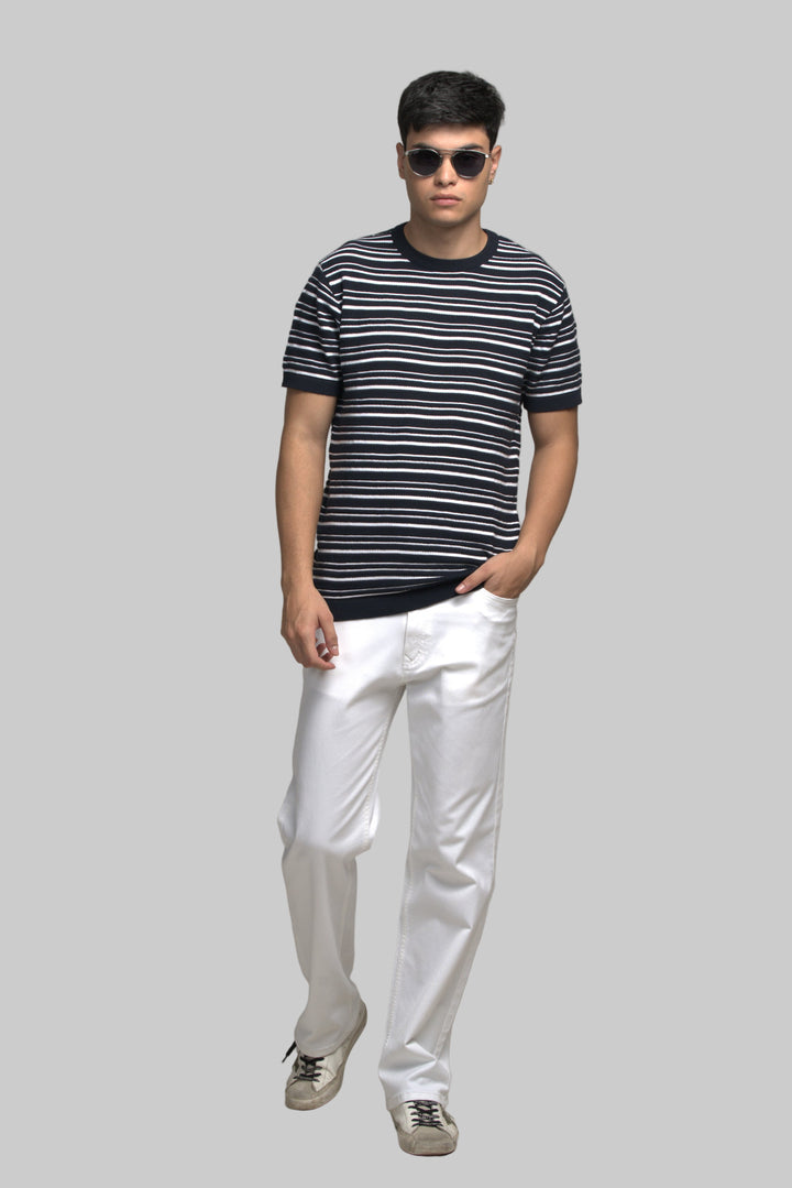 Man wearing a striped shirt and white pants against a plain background
