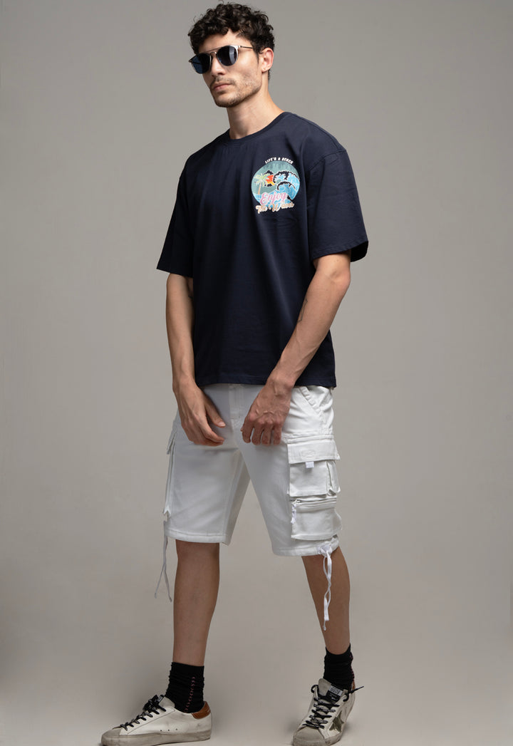Man wearing a navy t-shirt with a graphic design and white cargo shorts on a gray background